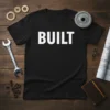 Black t-shirt with the bold white word "BUILT" and surrounding gears, wrench, and blueprints