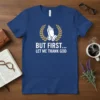 Blue t-shirt with white text "BUT FIRST... LET ME THANK GOD" and praying hands graphic with laurel wreath