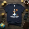 Dark navy t-shirt with "BUY BITCOIN YOU'RE WELCOME" text and a rocket launching over city buildings, featuring bitcoin symbols