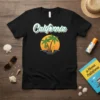 Black t-shirt featuring the word "California" in retro script, with a sunset, palm trees, and a surfboard graphic