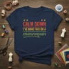 Navy blue t-shirt with "CALM DOWN I'VE DONE THIS ON A mannequin" text in red, white, and green typography
