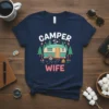 Camper Wife t-shirt design with a vintage camper, trees, flowers, and campfire graphic. Features "CAMPER" above and "WIFE" below the