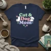 Cat & Dog Mom text with illustrations of a cat and dog, surrounded by paw prints, on a navy t-shirt