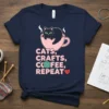 Navy t-shirt with "CATS, CRAFTS, COFFEE, REPEAT" text, featuring a cat in a coffee cup and knitting yarn graphic