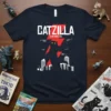 CATZILLA 注意危険な猫 T-Shirt featuring a silhouetted cat monster attacking a city with helicopters, red lightning bolts, and Japanese text