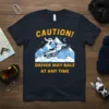 Snowmobile t-shirt with yellow text "CAUTION! DRIVER MAY BALE AT ANY TIME" and graphic of snowmobiler mid-air