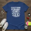 Blue t-shirt with white text "CAUTION! MAY SPONTANEOUSLY START DANCING" and dancing silhouettes graphic