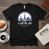 Black t-shirt with "c'est la vie" text, Eiffel Tower, coffee cup, and croissant graphic in purple and teal
