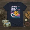 Charlie Don't Surf quote with retro helicopters and surfer on a wave graphic, pink and purple sunset, navy t-shirt