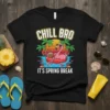 Black t-shirt design with "CHILL BRO IT'S SPRING BREAK" text, featuring a flamingo on an inflatable float in the ocean