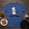 Chris P. Bacon text with a cartoon chef pig holding a frying pan with bacon on a blue t-shirt