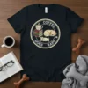 Coffee Dogs Naps circular design on a black t-shirt, featuring coffee cup, books, and sleeping dog graphic