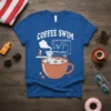 Blue t-shirt with "Coffee Swim" text, featuring a cartoon coffee maker brewing into a large mug where tiny people are
