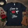 Como La Flor t-shirt design with white script text, red rose, and white hummingbird graphic