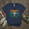 Navy blue t-shirt with "Congrats You Did It" text in orange and blue, framed by a laurel wreath and topped