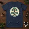 Conifer Ancient Evergreen T-Shirt featuring a stylized pine tree graphic with roots and text