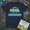 Navy t-shirt with "COOL LIKE MY GODPARENTS" text in yellow and blue, featuring sunglasses and a crown graphic