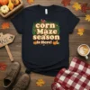 Corn Maze Season Is Here! text with pumpkins and corn stalks graphic on a navy t-shirt