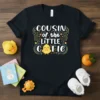 Black t-shirt with "COUSIN of the LITTLE CUTIE" text and a yellow chick graphic, decorated with colorful swirls and stars