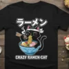 Black t-shirt with a cartoon black cat wearing a headband, eating ramen noodles with chopsticks. Text reads "Crazy Ramen Cat"