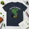 T-shirt design with white text "CREATE YOUR OWN GREEN" above a swirling green leaf tornado, with a silhouette painting the