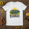 White t-shirt with "CREATE your own SUNSHINE" text and a vibrant sunflower field graphic, sun rays above