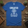 White text "CREATED WITH A PURPOSE" on blue t-shirt with graphic of a tree growing from an open book