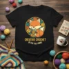 Black t-shirt with "Creative Crochet By Fox Tail Yarns" text and a cartoon fox holding yarn and crochet hooks