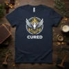 Navy blue t-shirt with a white and gold phoenix rising from flames, text reads "CURED"