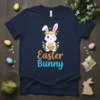 Navy blue t-shirt featuring the text "Easter Bunny" with a cute cartoon bunny holding an egg basket, surrounded by flowers