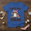 Blue t-shirt with "CUTE BUT FERAL" text and a cartoon raccoon holding a donut