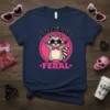 Cute But Feral text with a cartoon raccoon wearing star sunglasses and a bow tie on a navy t-shirt