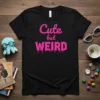 Black t-shirt with pink dripping text "Cute but WEIRD" graphic design, ideal for expressing a quirky personality
