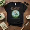 Black t-shirt with "DAISY" text above a circular graphic of a daisy flower surrounded by green vines and a blue