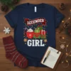 December Girl graphic tee with hot cocoa, presents, candy canes, and festive lights, celebrating a winter birthday