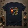 A black t-shirt with the number 12 designed in a colorful, geometric, and ethnic pattern, featuring a sun graphic