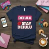 Navy t-shirt with "DELULU #STAY DELULU" text in pink and white bubble font, representing the trending meme