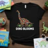 Black t-shirt featuring a floral dinosaur design with the text "DINO BLOOMS" below