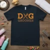 Dog Groomer T-Shirt featuring bold orange "DOG" with scissors and comb graphic, and brown "GROOMER" text below