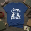 White "dog person" text with paw prints and three cartoon dogs sitting below on a navy blue t-shirt