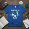 Blue t-shirt with "DON'T BE SO NaCl" text, featuring science graphics like beakers, test tubes, and periodic table elements for