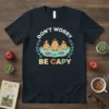 Don't Worry Be Capy t-shirt design with three cute capybaras in water, birds, and lotus flowers