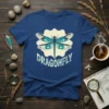 A blue t-shirt featuring a stylized dragonfly graphic with the word "DRAGONFLY" below, on a cream-colored background