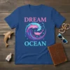 DREAM OCEAN text with pink dolphins swimming in a blue and purple wave, t-shirt design