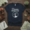 Navy t-shirt with white text "Dream WITHOUT FEAR" and a circular graphic of a person on a mountain peak reaching