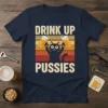 Drink Up Pussies t-shirt with a black cat holding two beer mugs, vintage sunset background, text "DRINK UP PUSSIES"