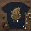 E T text graphic with a stylized alien character wearing a hat and holding a flower, dark t-shirt design