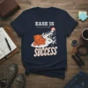 Ease Is The Greatest Success quote on a navy t-shirt with graphic of an armchair on clouds with mountain path