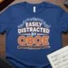 Easily Distracted By Oboe text design with musical notes and an oboe graphic, displayed on a blue t-shirt
