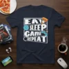 Eat Sleep Game Repeat t-shirt with gaming controller, pizza slice, and sad face graphic